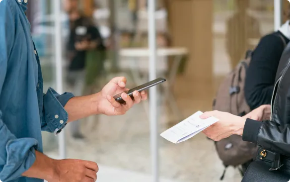 Person, die einer anderen Person einen ausgedruckten Geldschein übergibt und dabei ein Smartphone in der Hand hält, veranschaulicht die Verwendung von Thermokartendruckern und Geldscheinen.