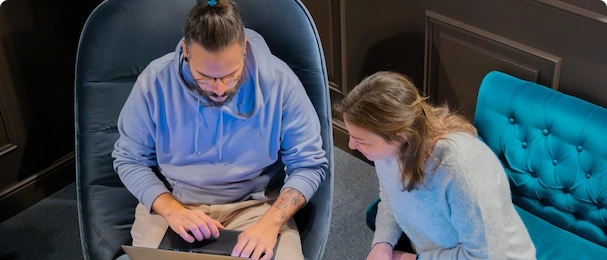 Zwei Berufstätige, die mit Laptop in einem modernen Arbeitsbereich an einem Projekt arbeiten.