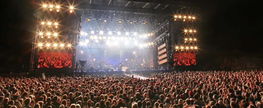 Foule dense devant une scène illuminée lors d'un concert en plein air, mettant en avant des tarifs avantageux pour la billetterie.