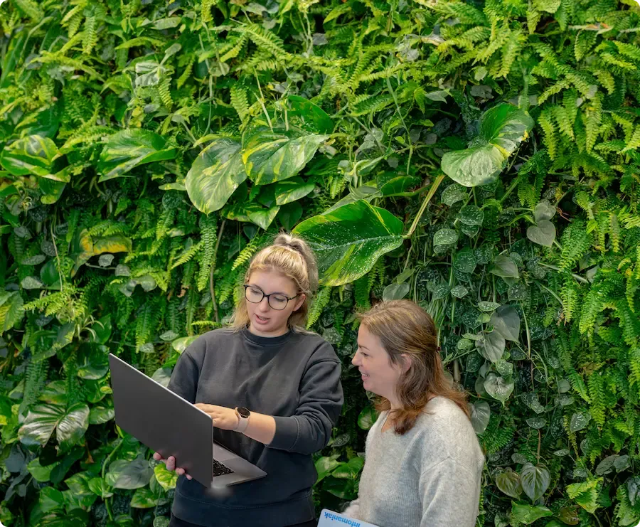 Image of two employees in front of a plant wall