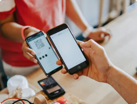 Person, die ein Smartphone benutzt, um einen QR-Code auf einem anderen Telefon zu scannen, symbolisiert einen modernen, digitalen Verkaufsschalter.