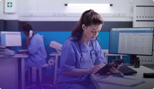 Image of a nurse consulting a digital device in a hospital room equipped with various monitors and computers, reflecting daily activity in the medical sector.